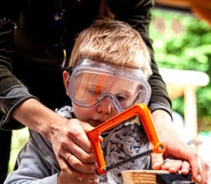 Close up of a boy being helped to saw wood in a vice