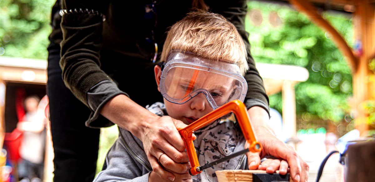 Close up of a boy being helped to saw wood in a vice