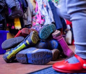 A pile of wellington boots with an child wearing indoor shoe in the foreground