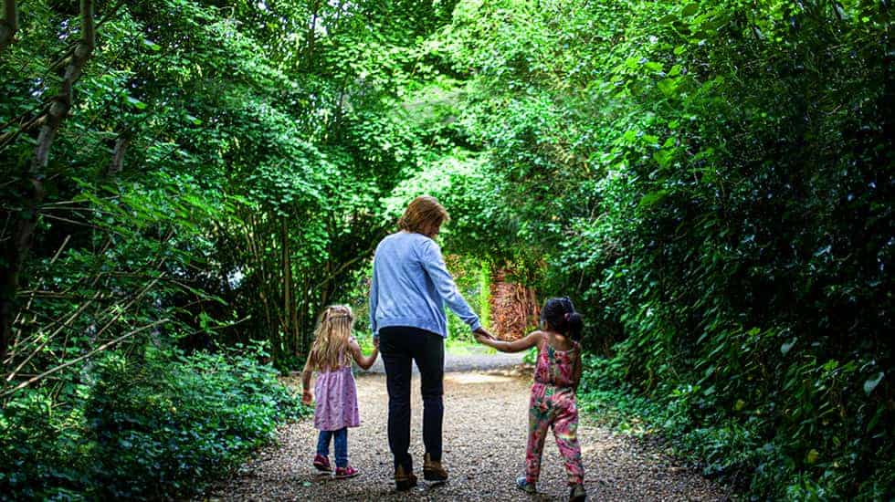 An adult with two children walking down Millington Road Nursery School leafy lane entrance
