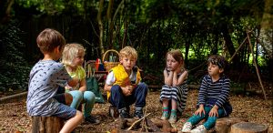 Five children sitting round unlit wood pile campfire