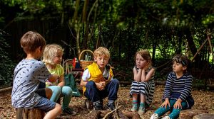 Five children sitting round unlit wood pile campfire