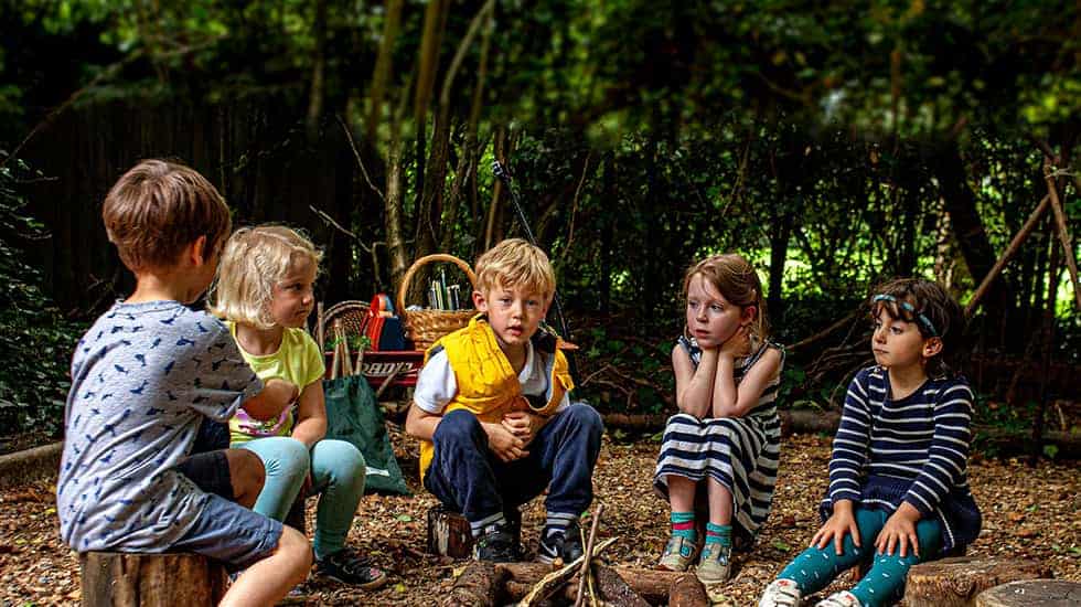 Five children sitting round unlit wood pile campfire 